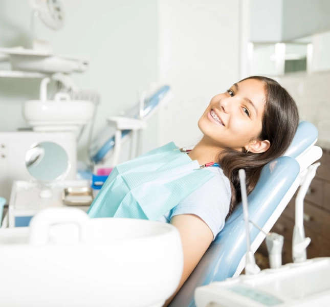Child smiling while sitting in a dental chair during a dental appointment.
