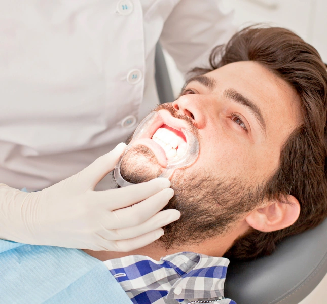 Clinician in white gloves adjusting a clear cheek retractor on a man reclining in a treatment chair