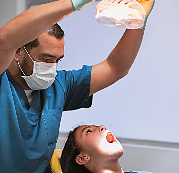 Clinician adjusting an overhead light during a dental examination of a young patient with an open mouth