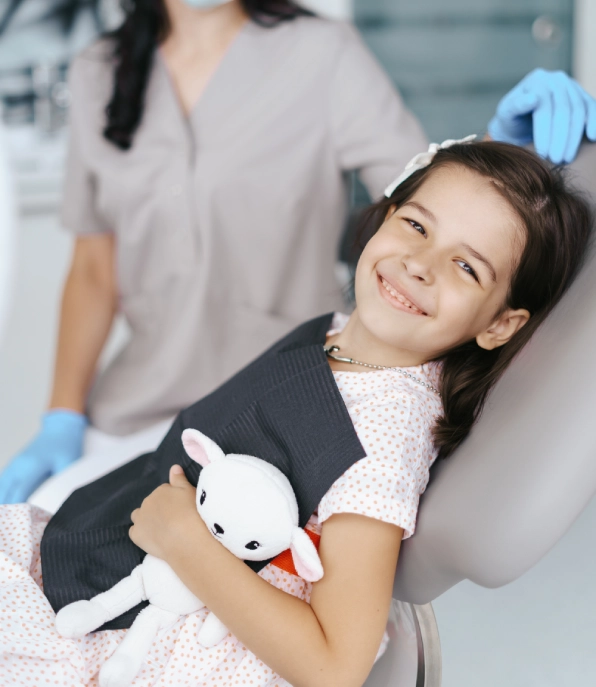 Clinician in scrubs and face mask giving a thumbs-up alongside a boy in a dental chair