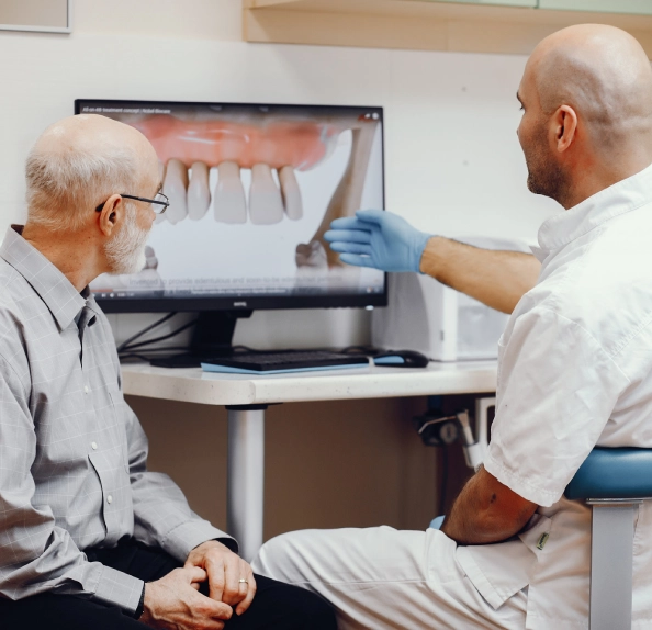 Clinician pointing to a 3D dental model display on a computer screen while talking with an older man