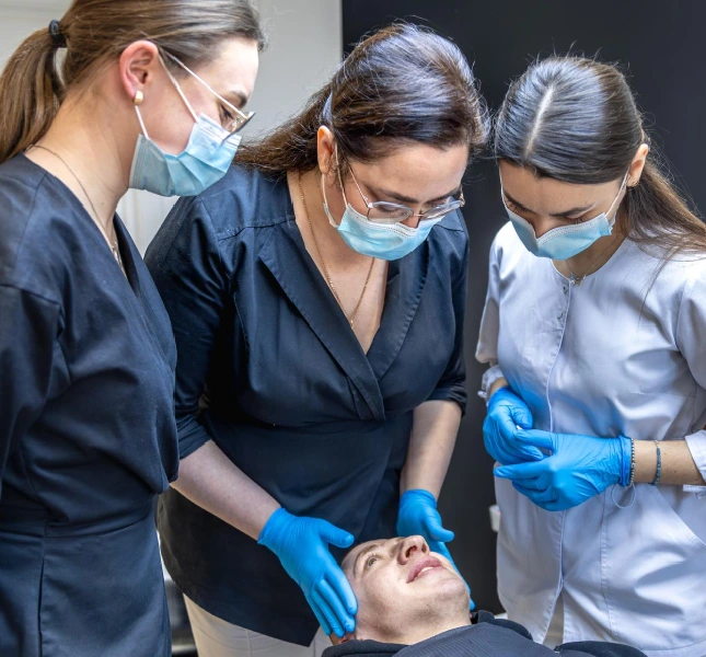 clinicians examining a person seated in a dental chair during a dental procedure.