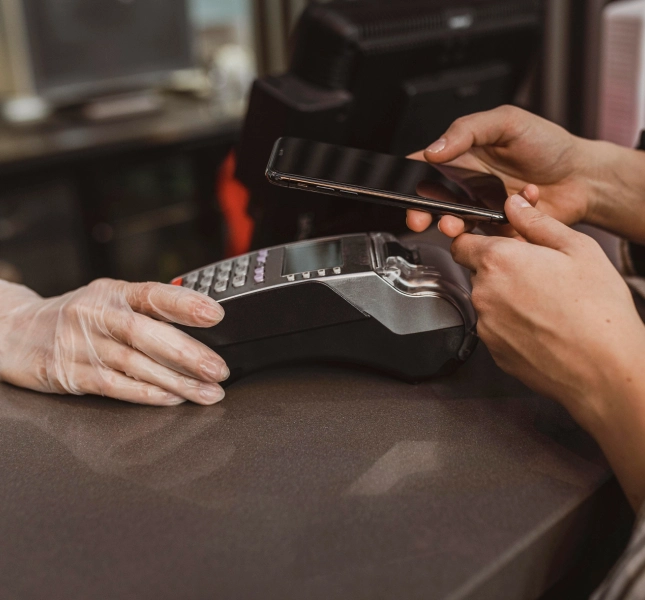 Person tapping a smartphone against a payment terminal held by a gloved hand