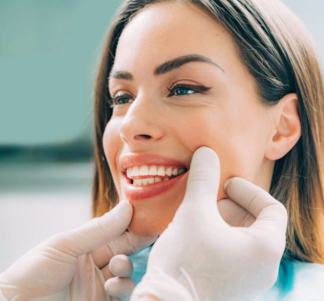 Gloved hands holding the cheeks and chin of a smiling woman during an examination