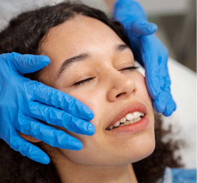 Gloved hands performing a facial and jaw examination on a woman with closed eyes