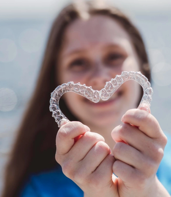 Hands holding two clear dental aligners together to form a heart shape