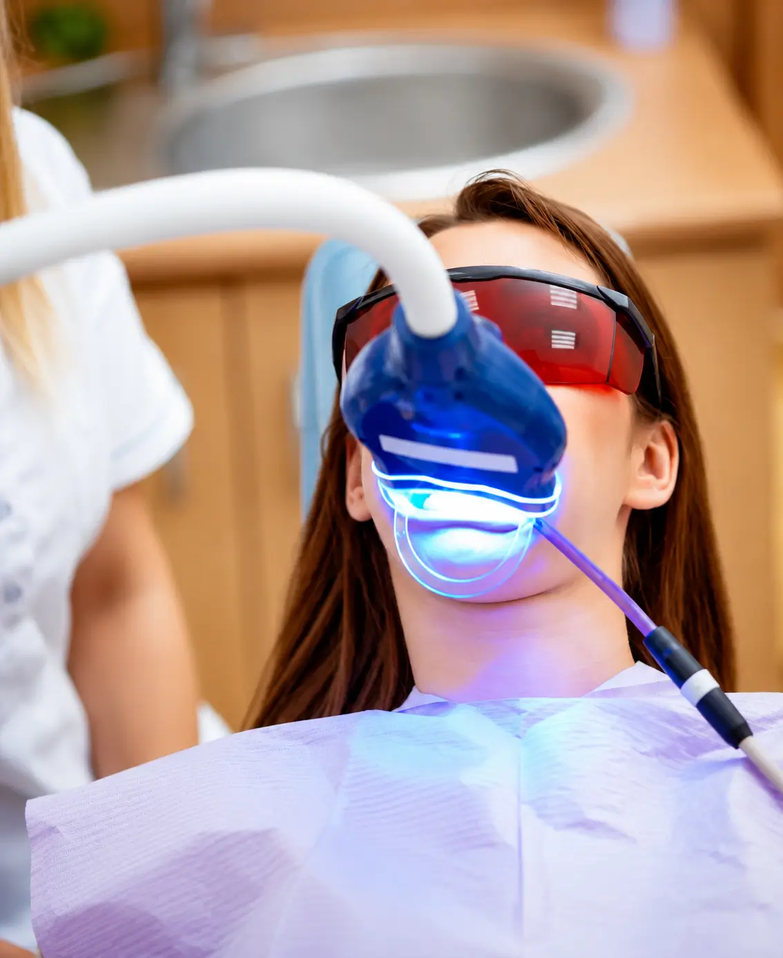 Patient undergoing an in-chair LED teeth whitening treatment while wearing protective glasses
