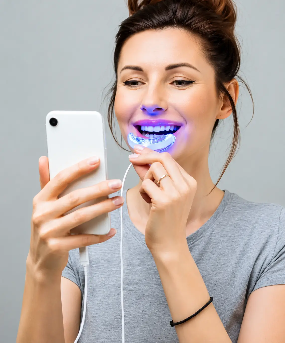 Person using an LED teeth whitening mouth tray while looking at a phone