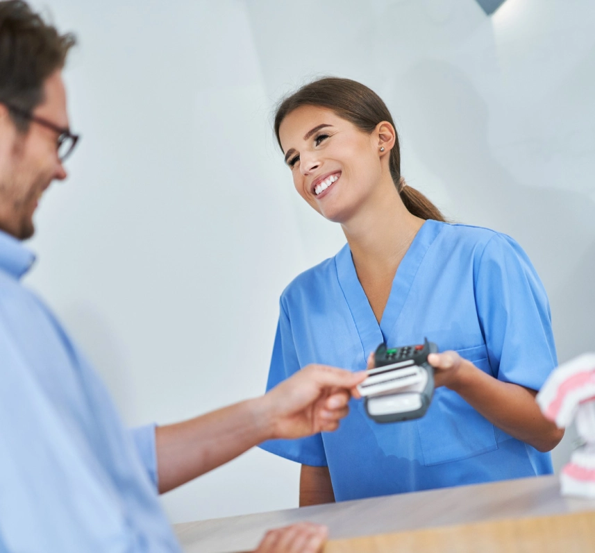 Man tapping a card on a payment terminal held by a smiling staff member in blue scrubs