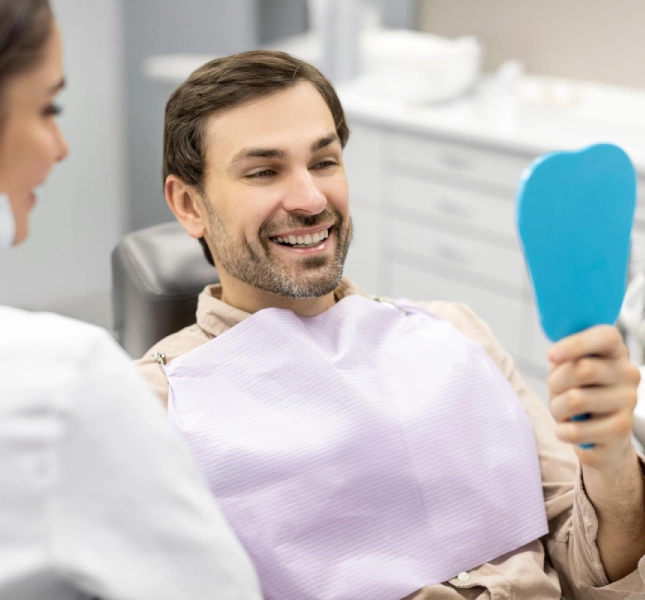 Patient smiling while looking at their smile in a hand mirror after a dental appointment.