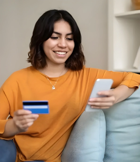 Person holding a payment card while using a smartphone at home.
