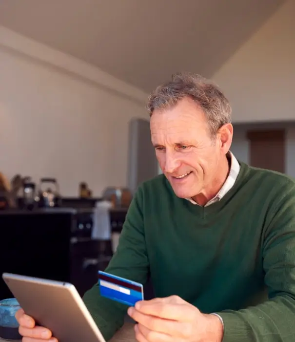 Person holding a payment card while using a tablet at home.