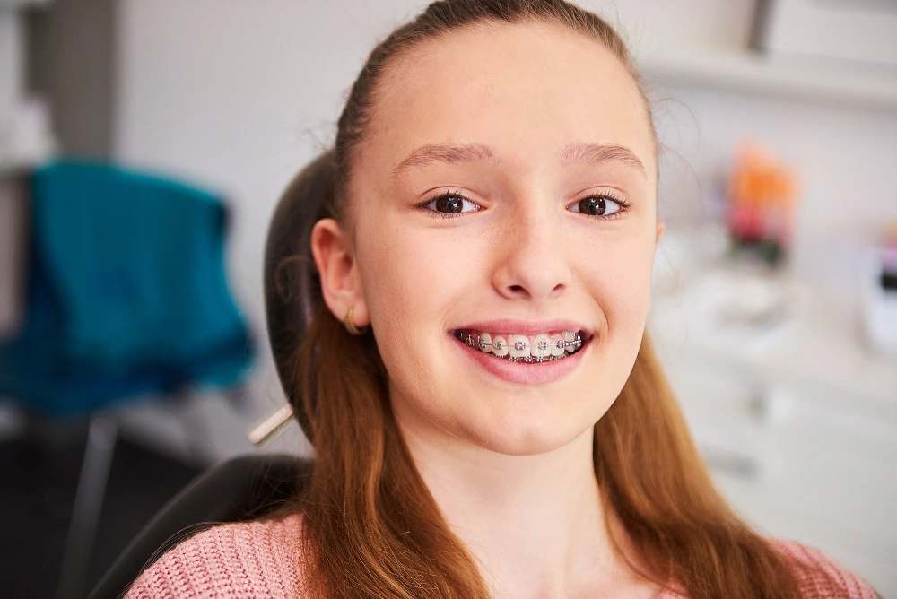 Smiling young girl sitting in a dental chair wearing metal braces