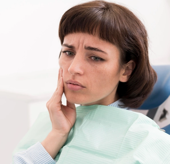 woman holding hand to cheek dental chair