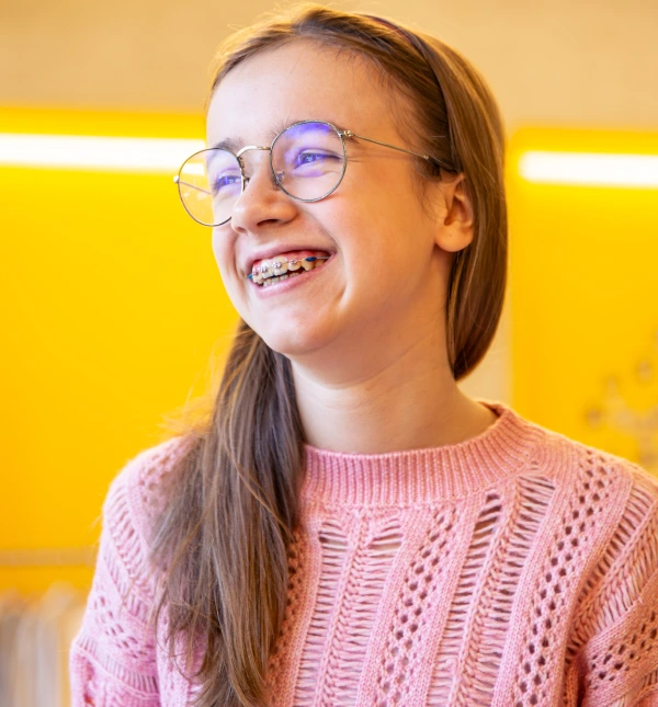 Young girl with glasses smiling widely wearing metal dental braces