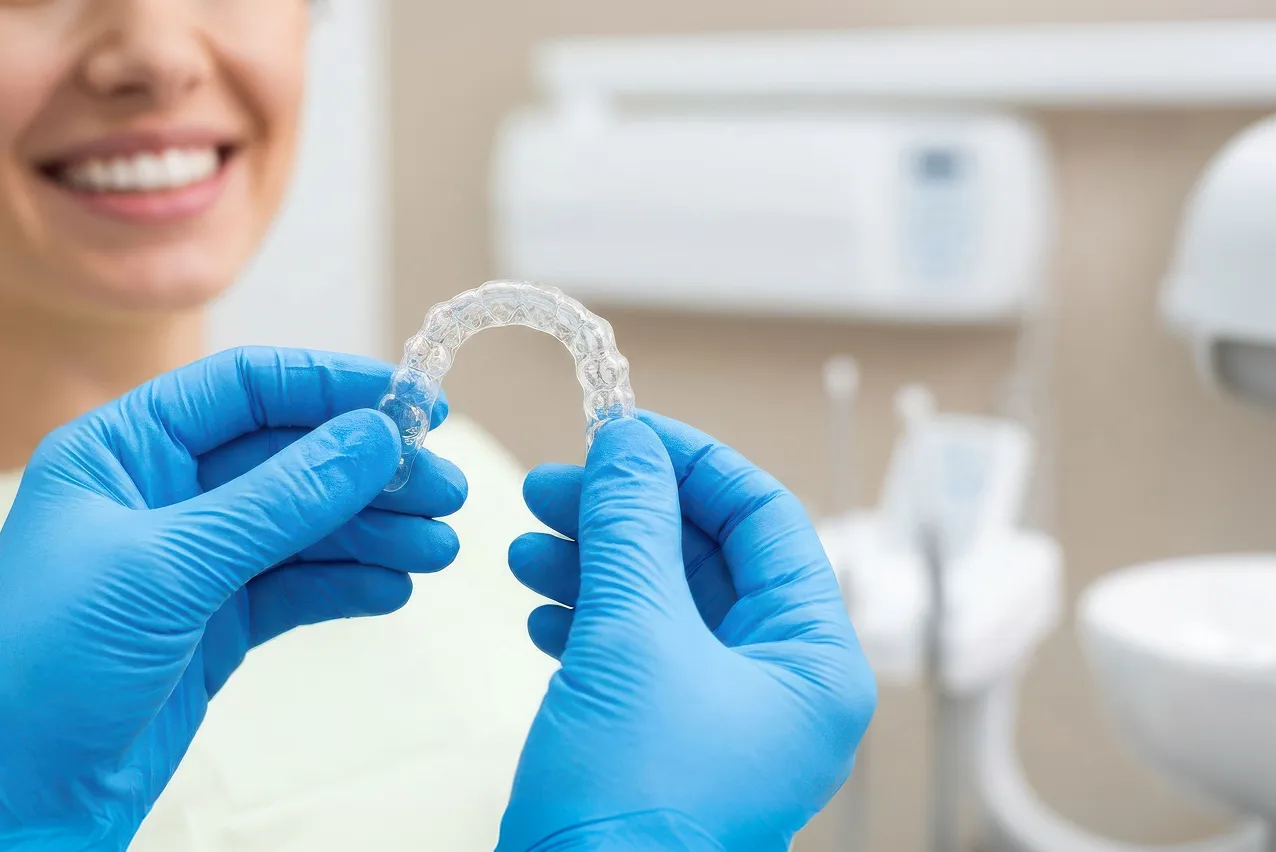 Clear dental aligner held by gloved hands