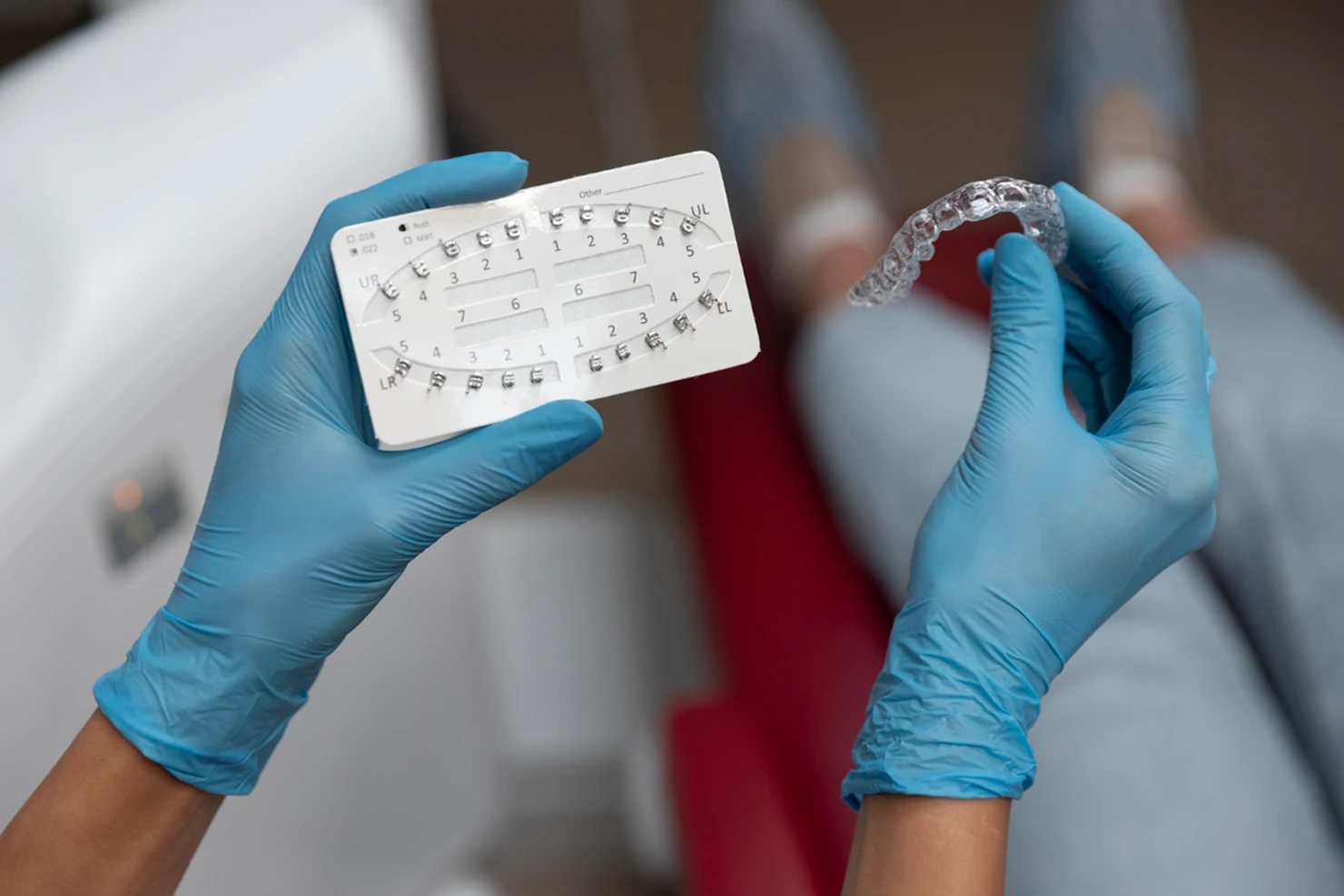 Gloved hands holding orthodontic brackets and a clear dental aligner