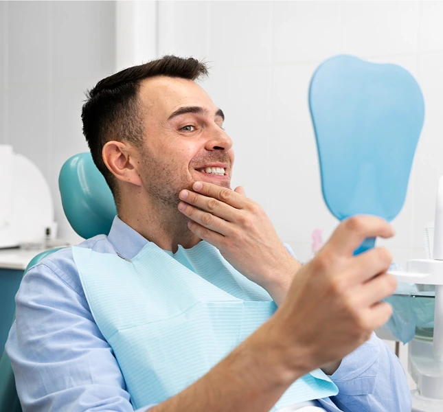 Man seated in a dental chair checking his teeth in a hand mirror