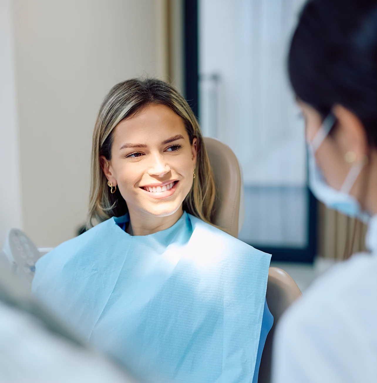 Woman seated in a dental chair speaking with a dentist.