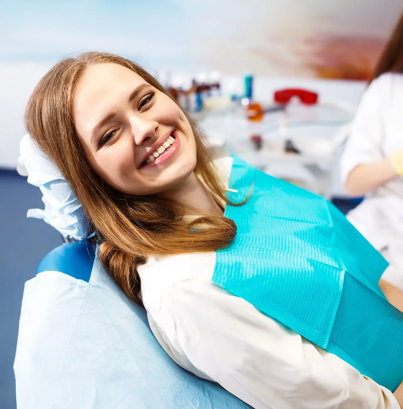 Woman smiling in a dental chair wearing a blue dental bib